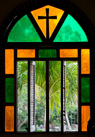 A stained glass window frames a view of palm trees outside the chapel at Camp Canaan, a Methodist retreat center near Santa Clara, Cuba. Photo by Mike DuBose, UMNS.