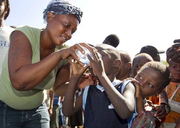 Sharlene Jean offers a sample of treated drinking water to a child living in a makeshift camp in Gresier, Haiti. The United Methodist Committee on Relief and partner agencies provided water treatment supplies to the camp. Photo by Mike DuBose, UMNS.