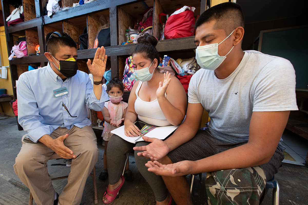 The Rev. Joel Hortiales (left) prays with Carlos Ivan Baran Hidalgo; his wife, Danelly Mazariegos Morales; and their 3-year-old daughter, Scarlett Juliette, at the Camino de Salvación shelter in Tijuana, Mexico. The family fled violence in Guatemala and is hoping to pursue a claim for asylum in the U.S. Hortiales is a United Methodist missionary and serves as director of Hispanic/Latino ministries and border concerns for the California-Pacific Conference. Photo by Mike DuBose, UM News.