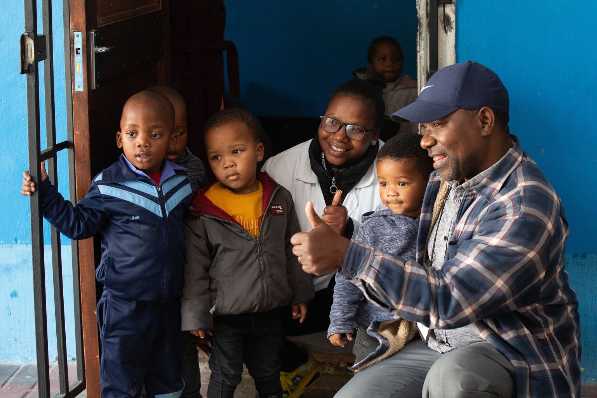 The Rev. Joao Sambo, right, interacts with students and a teacher at Nomaxabiso Centre in the Phillippi neighborhood of Cape Town, South Africa. Sambo, who coordinates Lusophone coverage for UM News, helped lead training for communicators from the South Africa Provisional Conference. (Photo by Mike DuBose, UM News.)