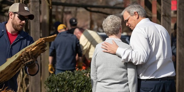 Bishop William McAlilly (right) comforts the Rev. Judi Hoffman in the park outside East End United Methodist Church in Nashville, Tenn., while volunteers clean up debris from a tornado that heavily damaged the church's sanctuary and offices. (Photo: Mike DuBose, UM News.)