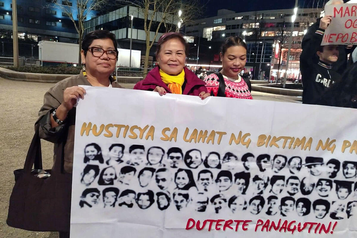 (From left) United Methodist Deaconess Rubylin G. Litao, Nay Llore Pasco, a leader of the Rise Up for Life and for Rights network, and lawyer Krissi Conti, International Criminal Court-accredited assistant to the counsel of the victims’ families, hold a banner with the faces of victims at a rally in the International Criminal Court at The Hague in the Netherlands on Feb. 25. Photo courtesy of Rubylin Litao.