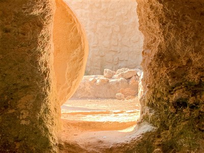 View from inside an empty stone tomb, with light streaming through the entrance