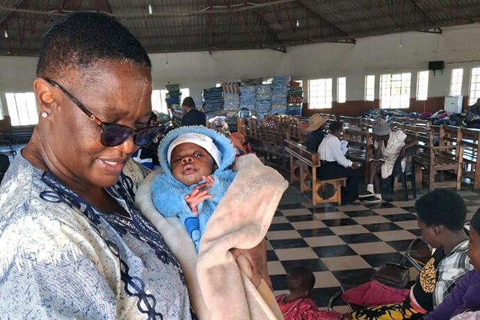 La pasteure Heather J. Zisengwe, surintendante du district de Bulawayo Midlands de l’Église Méthodiste Unie au Zimbabwe, tient un bébé dans ses bras dans un camp de transit mis en place par le Conseil des Églises du Zimbabwe pour les migrants qui ont quitté l’Afrique du Sud en raison des manifestations anti-immigration. Ce centre temporaire, installé dans le sanctuaire de l’Église unie du Christ en Afrique australe à Njube, a servi de plaque tournante aux efforts humanitaires menés par les Églises traditionnelles du Zimbabwe. Photo gracieusement fournie par la pasteure Heather J. Zisengwe.