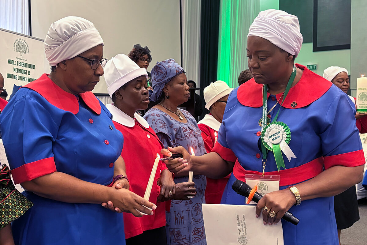 Patricia Petudzai Mapani lights a candle held by Tabitha Mushishi, The United Methodist Church in Zimbabwe’s unit coordinator, during a memorial service for members of the World Federation of Methodist and Uniting Church Women in Botswana in April 2025. Photo by Eveline Chikwanah, UM News.